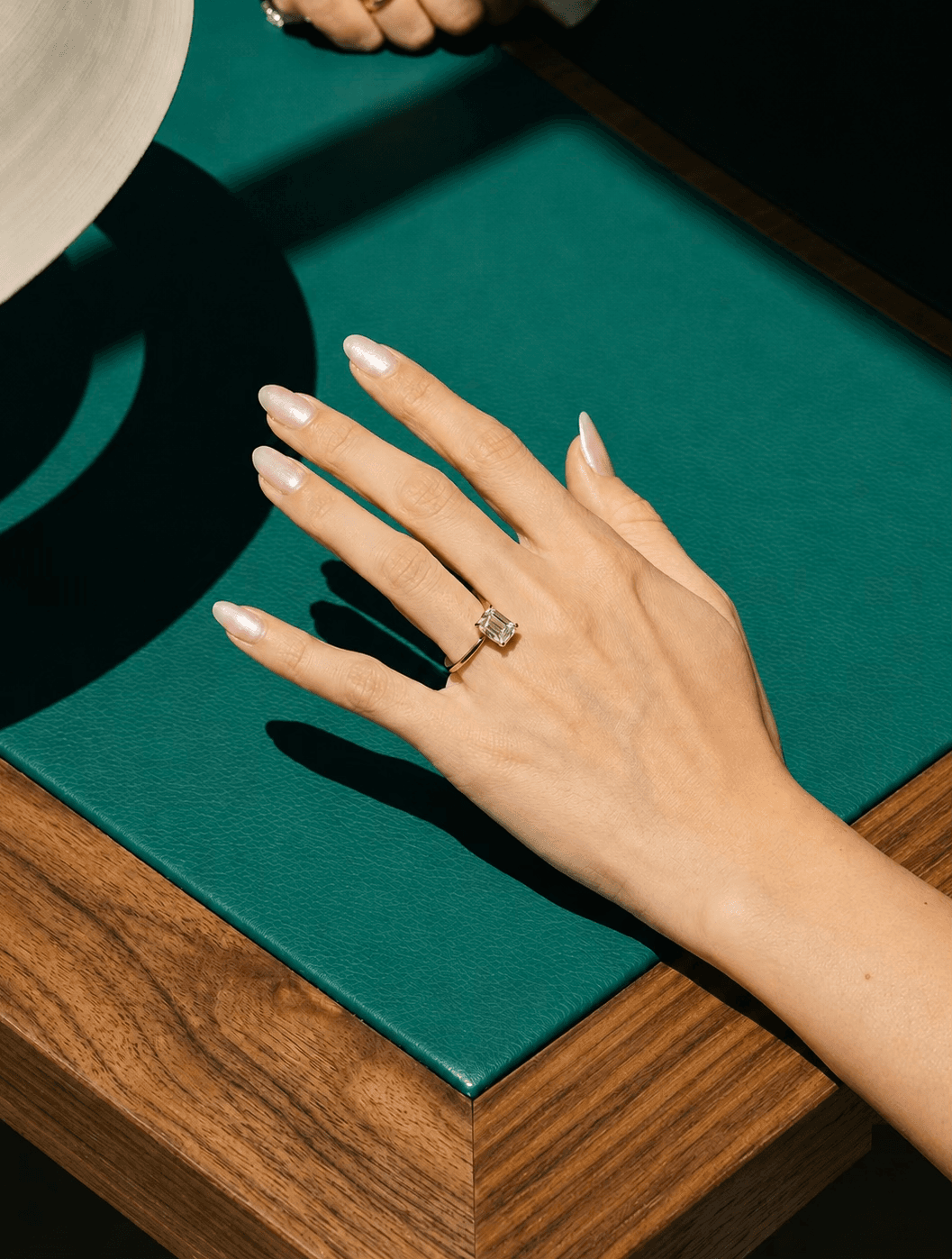 Hand wearing an engagement ring on teal leather display at MOH London showroom