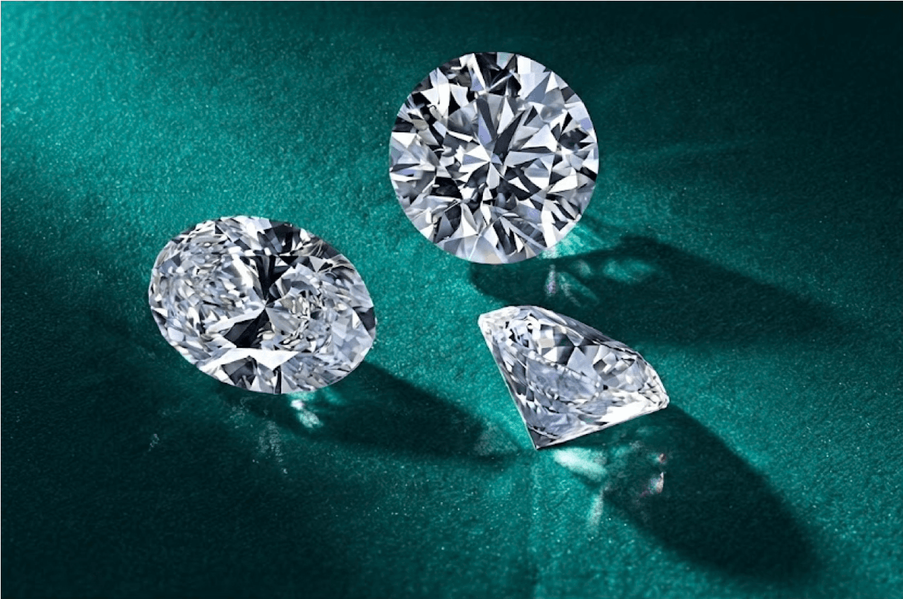 Three loose diamonds — round, oval, and pear — displayed on teal surface